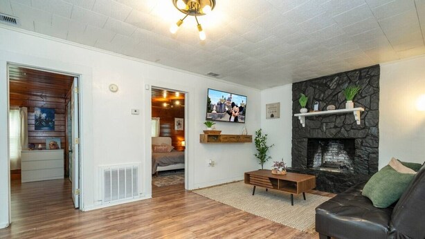 A living room with a fireplace, a sofa, a TV, and a wooden floor. - The Cozy Corner House (Kissimmee)