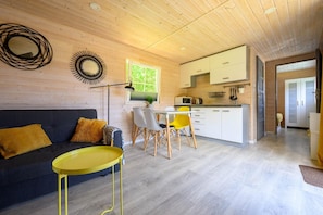A modern interior with a wooden ceiling, a dining area with yellow chairs, a kitchen with white cabinets, and a sofa with yellow pillows.