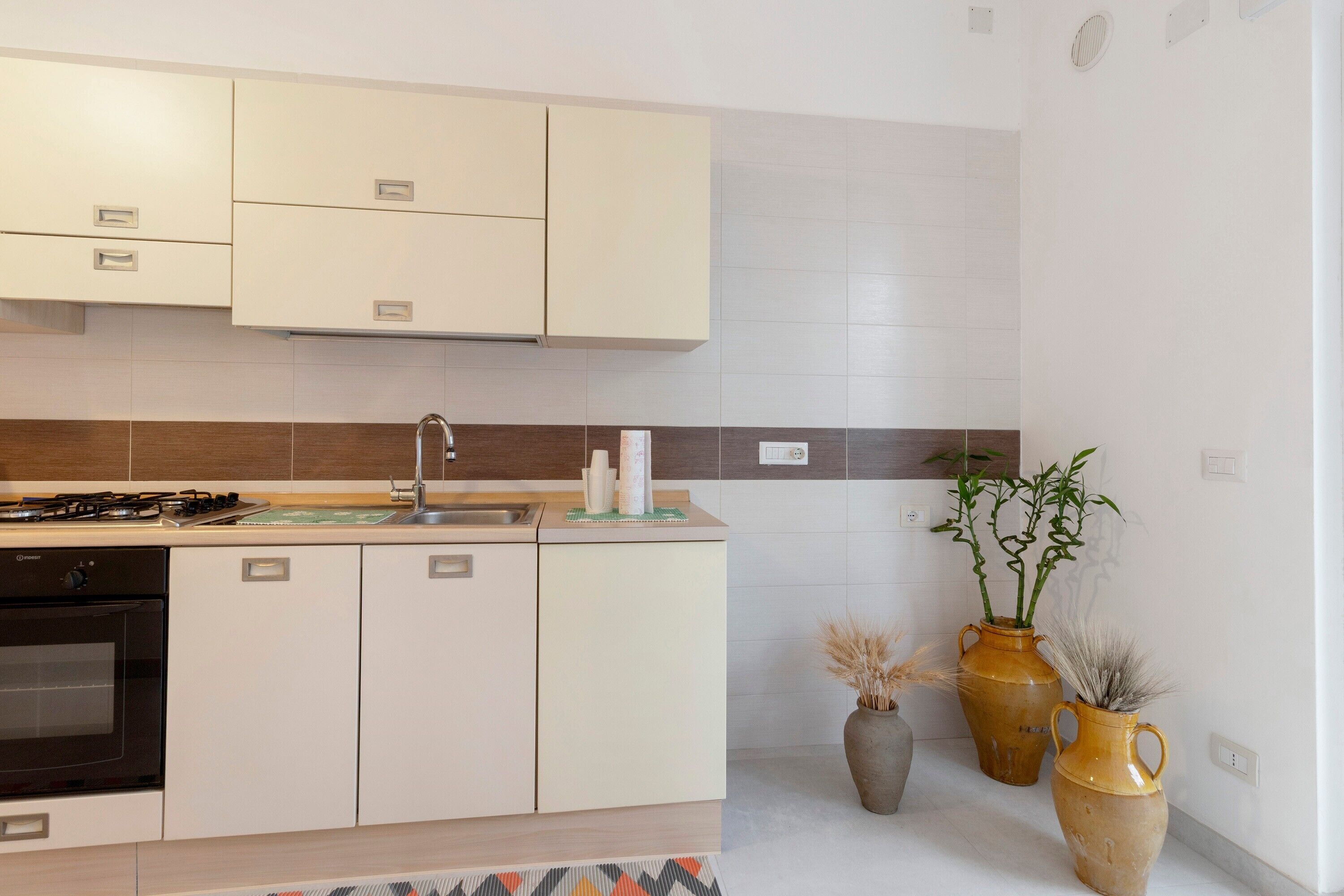 A modern kitchen with white cabinets, a gas stove, a sink, and two large vases with plants.