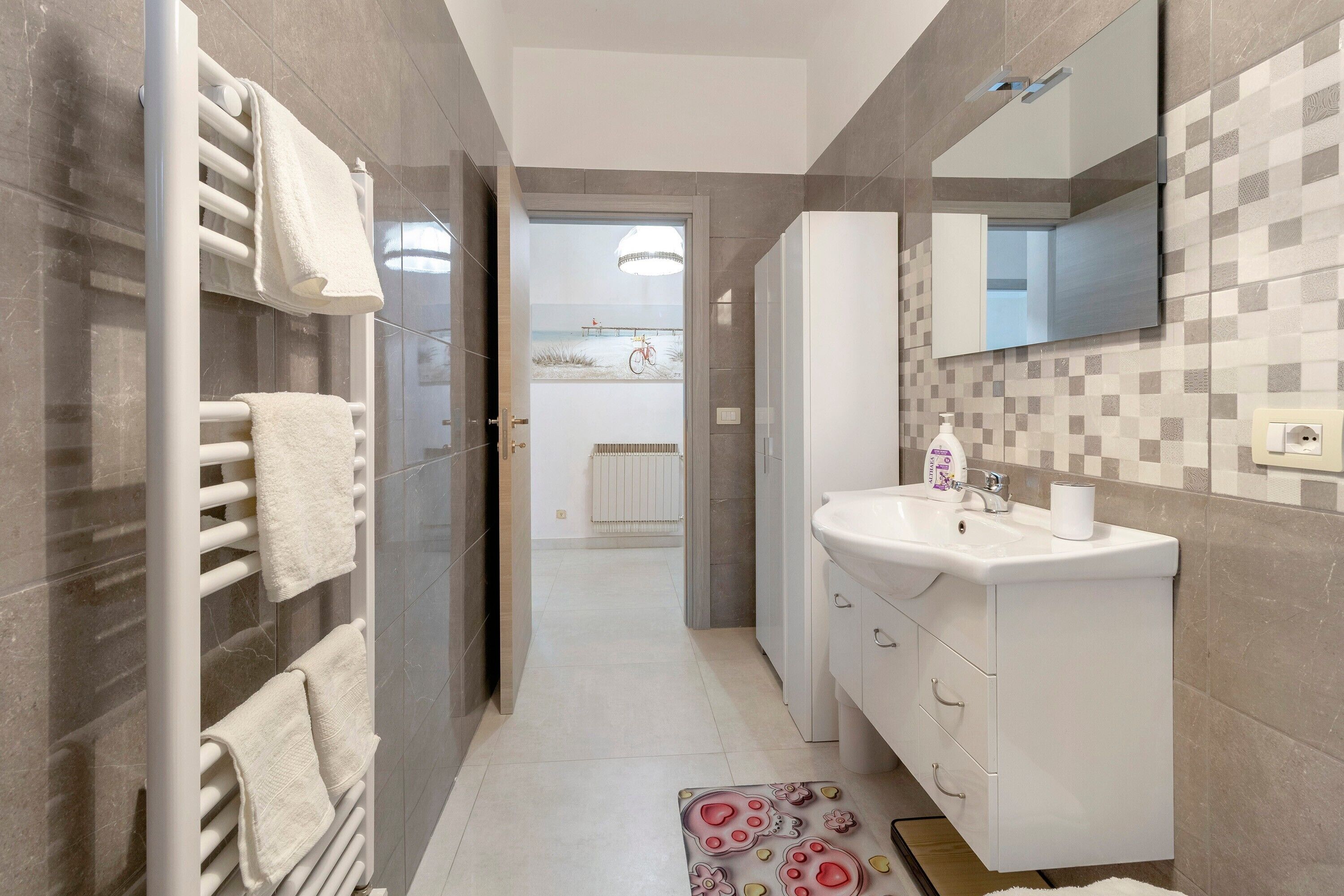 Un bagno moderno con lavandino, specchio e porta asciugamani bianchi.