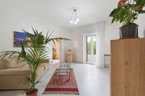 Un salon moderne avec un canapé, une table basse en verre, un tapis à motifs rouges, une plante en pot et un tableau accroché au mur.