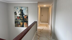 En hall med ett marmorgolv, ett träräcke och en målning som föreställer en stadsbild.