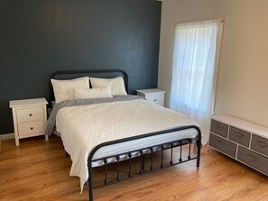 Ein Schlafzimmer mit einem Bett, zwei Nachttischen, einer Fensterbank, einem Vorhangfenster und einer eingebauten Bank mit Schubladen.
