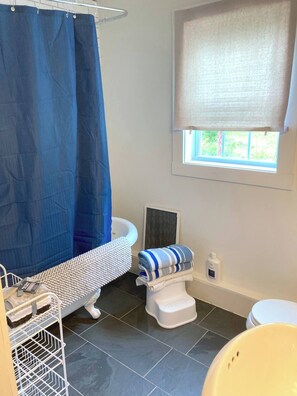 Ein Badezimmer mit Badewanne, Toilette und einem Fenster mit Blick auf Grünflächen.
