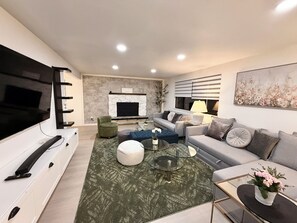 Een moderne woonkamer met een flatscreen televisie, een open haard, een bank en een salontafel.