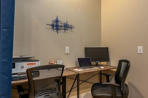 Un espacio de trabajo con escritorio, dos sillas, una computadora portátil, un monitor de escritorio y una impresora HP.