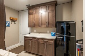 A compact kitchen with wooden cabinets, a black refrigerator, and a small blue trash bin.
