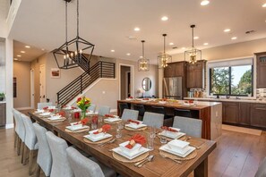 Cocina moderna con una isla central, mesa de comedor de madera dispuesta para seis comensales y una escalera que sube a un nivel superior.