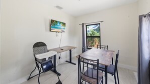 A room with a dining table, chairs, a high chair, a painting, and a window with a view. - Delightful 3-bedroom house with AC in West Palm Beach (West Palm Beach)
