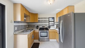 A compact kitchen with wooden cabinets, a stainless steel refrigerator, a built-in oven, and a granite countertop. - Delightful 3-bedroom house with AC in West Palm Beach (West Palm Beach)
