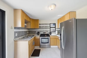 Eine kompakte Küche mit Holzschränken, einem Edelstahlkühlschrank, einem eingebauten Backofen und einer Arbeitsplatte aus Granit.