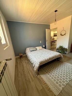 Ein Schlafzimmer mit einem Bett, einem Heizkörper, einem Holzboden, einem gemusterten Teppich und einer Decke mit linearer Gestaltung.
