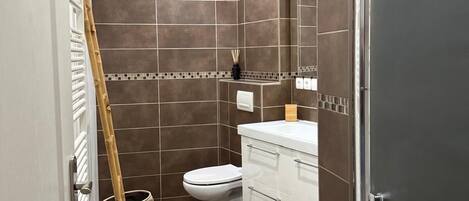 A bathroom with dark brown tiles, a white toilet, a white vanity, and a mirror.