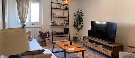 En moderne stue med sofa, sofabord, fjernsyn, reol og en hængende lampe.