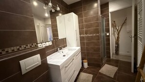 Un baño moderno con un espejo grande, muebles blancos, un lavabo y una zona de ducha.