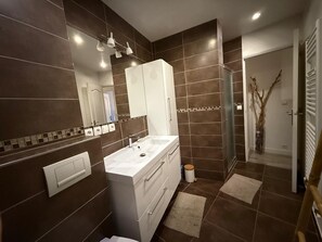 Ein modernes Badezimmer mit großem Spiegel, weißen Schränken, einem Waschbecken und einer Duschkabine.