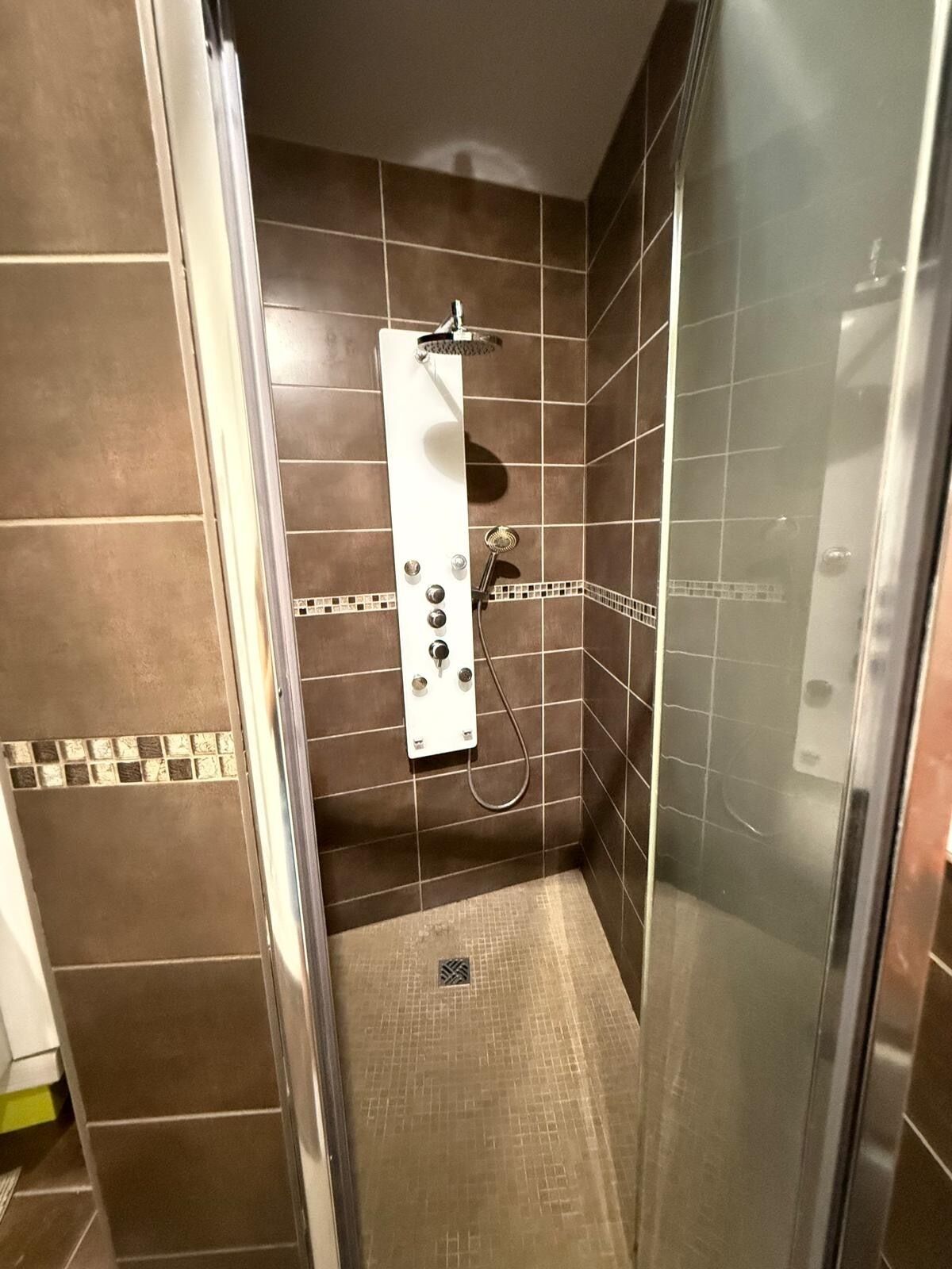 A shower stall with a handheld showerhead, a control panel, and a tiled floor.