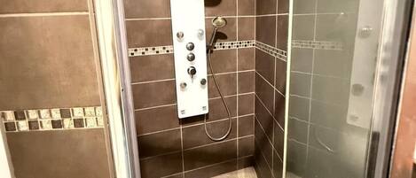 A shower stall with a handheld showerhead, a control panel, and a tiled floor.