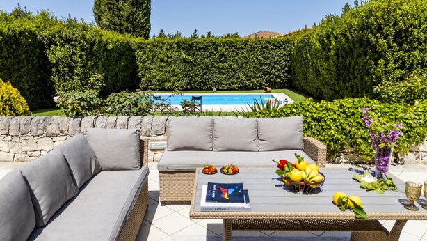 A patio with a sofa, table, and a pool in the background. - Villa Rebecca - Modica (Modica)