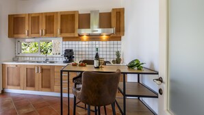 A kitchen with wooden cabinets, a stainless steel range hood, a tiled backsplash, a bar stool, and a bottle of wine on the counter. - Villa Rebecca - Modica (Modica)