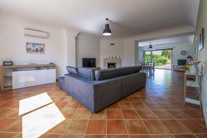 Een moderne woonkamer met een bank, televisie, open haard en een eethoek met stoelen.