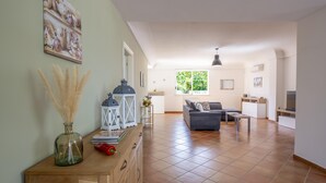 A spacious living area with a sofa, a coffee table, and a dining table. There is a window with a view of greenery, and a decorative vase on a wooden cabinet. - Villa Rebecca - Modica (Modica)