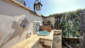 Un pequeño espacio al aire libre con un muro de azulejos, un farol de metal, un lavamanos y un azulejo decorativo.