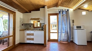 A kitchen with wooden cabinets, a gas stove, a microwave, and a window with a curtain. - Appartamento Miranda Oro - Caste... (Castellammare del golfo)