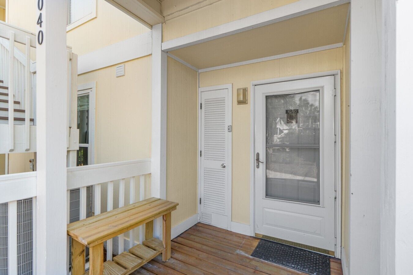 A wooden bench outside a building with a white door and a window with a frosted glass panel.