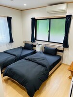 Una habitación con dos camas, una ventana con cortinas, un equipo de aire acondicionado y una pequeña mesa.