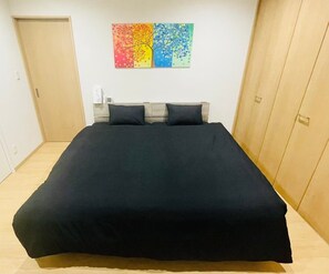 A bedroom with a bed, a wooden wardrobe, and a colorful wall art piece. - THE Erabu (Wadomari)