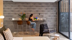 Ein modernes Zimmer mit Backsteinwand, einem Schreibtisch mit Laptop, einem Stuhl und einer Couch.