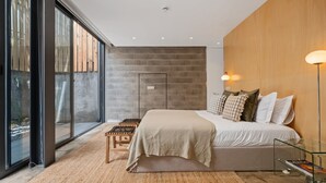 Ein modernes Schlafzimmer mit einem großen Bett, einer Holzwand als Akzent und Blick durch raumhohe Fenster.