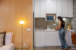A modern kitchen with white cabinets, a built-in microwave, and a person preparing food. - The 21 - Gaia by Homie (Ribeira Brava)