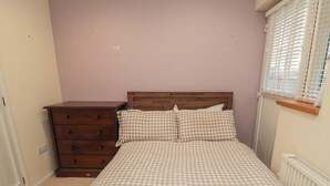 Une chambre avec une couvre-lit à carreaux, une commode en bois et une fenêtre avec des stores.
