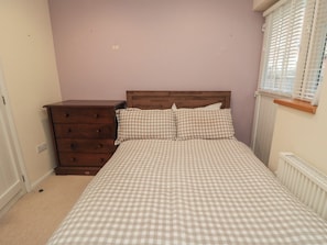 A bedroom with a checkered bedspread, a wooden dresser, and a window with blinds. - The Joinery (Scarborough)