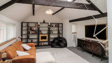 Une pièce de style loft avec des poutres apparentes, une cheminée, un canapé en cuir noir, un tapis blanc et un meuble en bois.