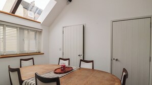 Une salle à manger avec une table ronde en bois, quatre chaises, une lucarne, une fenêtre avec des stores et une porte blanche.