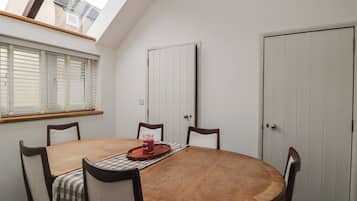 A dining room with a round wooden table, four chairs, a skylight, a window with blinds, and a white door.