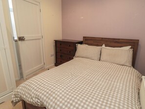 A bedroom with a checkered bedspread, a wooden dresser, and a door. - The Joinery (Scarborough)
