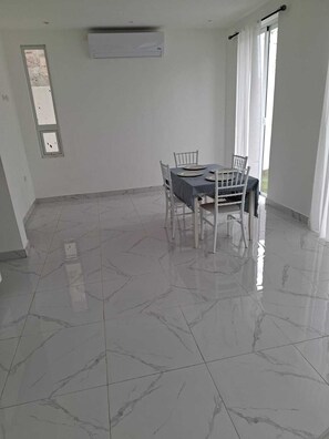 Un coin repas avec une table et des chaises, une fenêtre avec des rideaux et un appareil de climatisation fixé au mur.