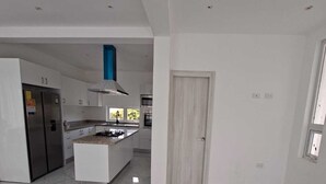 A modern kitchen with a central island, white cabinetry, and a blue range hood. - 3-bedroom house in charming Punta Cana with cool AC (Punta Cana)