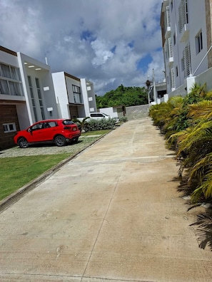 Une rue résidentielle bordée de maisons modernes, une voiture rouge garée sur le côté et un chemin piétonnier en béton.