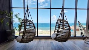 A room with large windows, two hanging chairs, a hammock, and a potted plant. - COCAZ0109 - Condominio LIT 760 (Salvador)