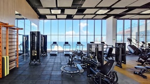 A gym with exercise equipment, a pull-up bar, and large windows overlooking a body of water. - COCAZ0109 - Condominio LIT 760 (Salvador)