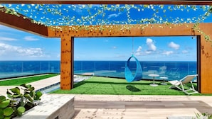 A modern outdoor lounge with a hanging chair, a small table, and a view of the ocean. - COCAZ0109 - Condominio LIT 760 (Salvador)