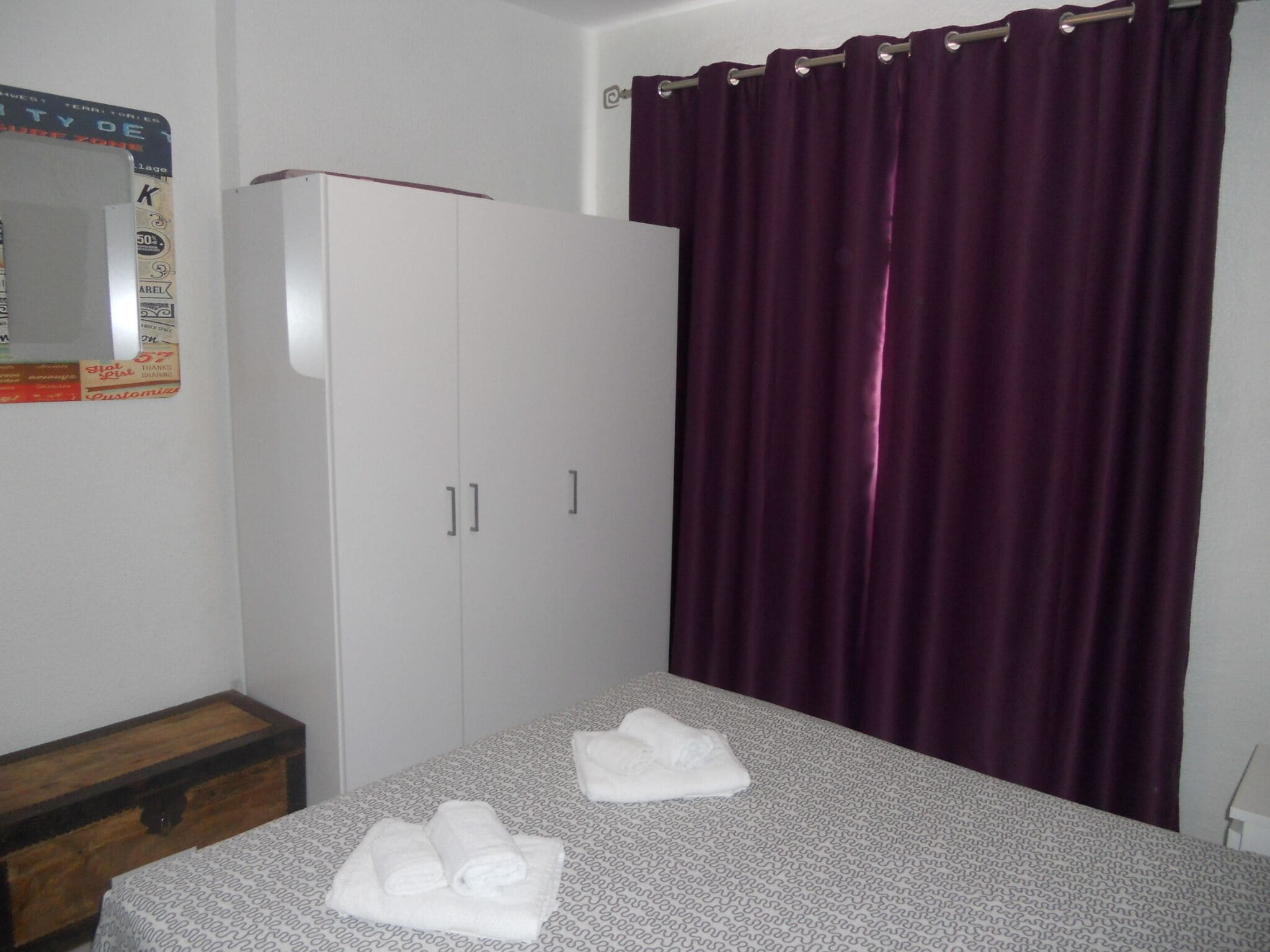 A bedroom with a bed, a wardrobe, a nightstand, and a purple curtain.
