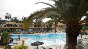 A swimming pool with lounge chairs and palm trees. - Lovely Apt Siesta (La Oliva)