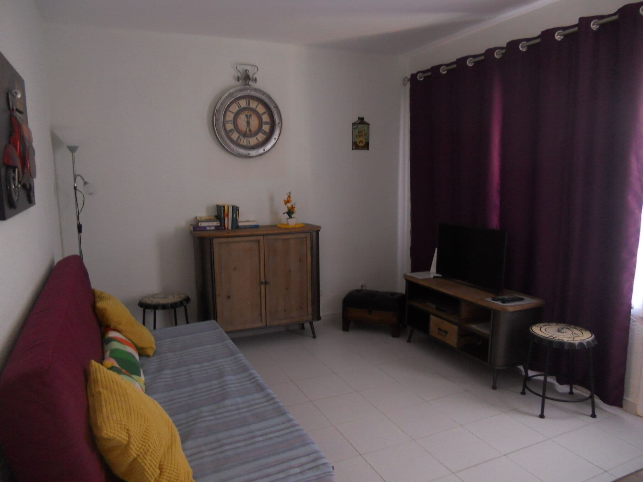 Een woonkamer met een bank, een kast, een televisie en een klok aan de muur.