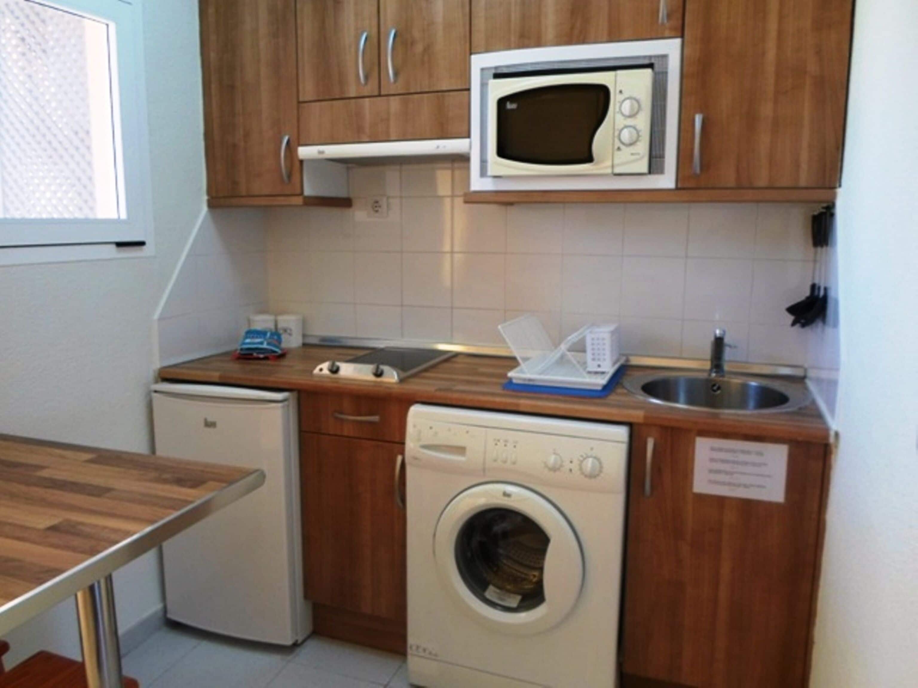 Une cuisine compacte équipée d’un four à micro-ondes, d’un lave-linge, d’un petit réfrigérateur et d’un évier.